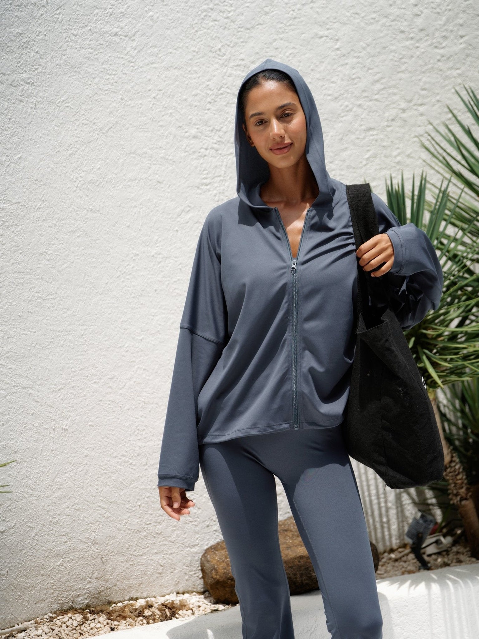 Modell med Balion Studio Flow Jacket Lunar Grey og hette oppe – bærer svart Balion tote bag utendørs