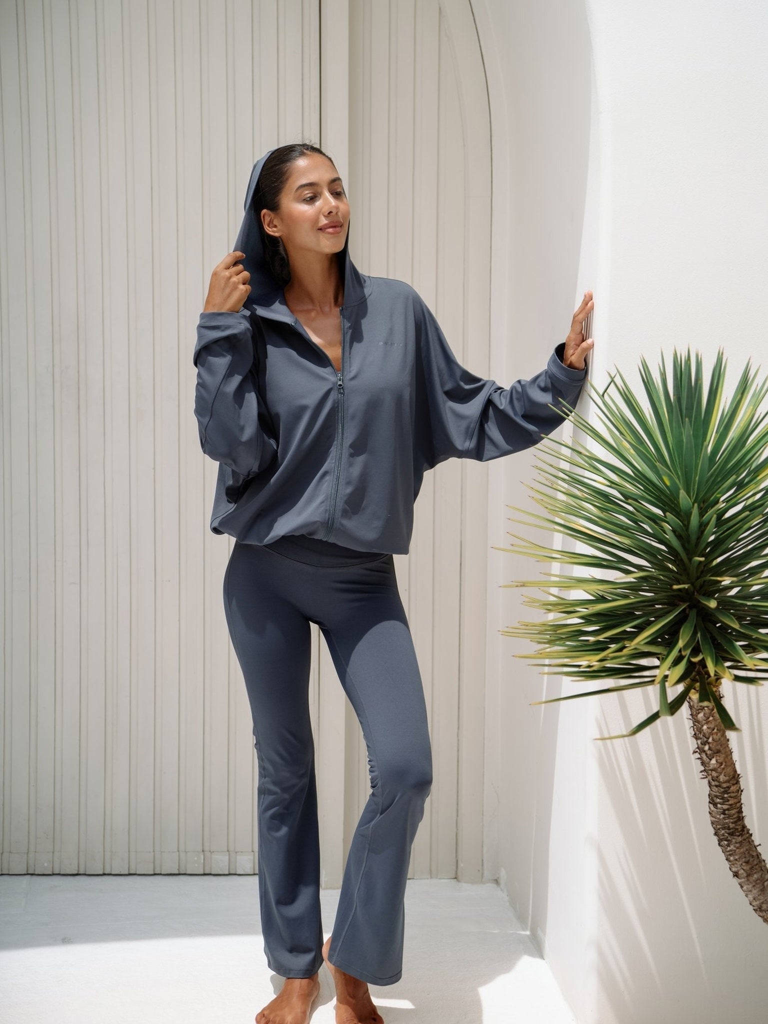 Balion Flare Tights Lunar Grey med hette-jakke – helfigur stående ved hvit bue og palmetre